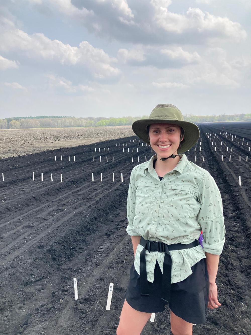 woman stands in field with hills and trees behind her